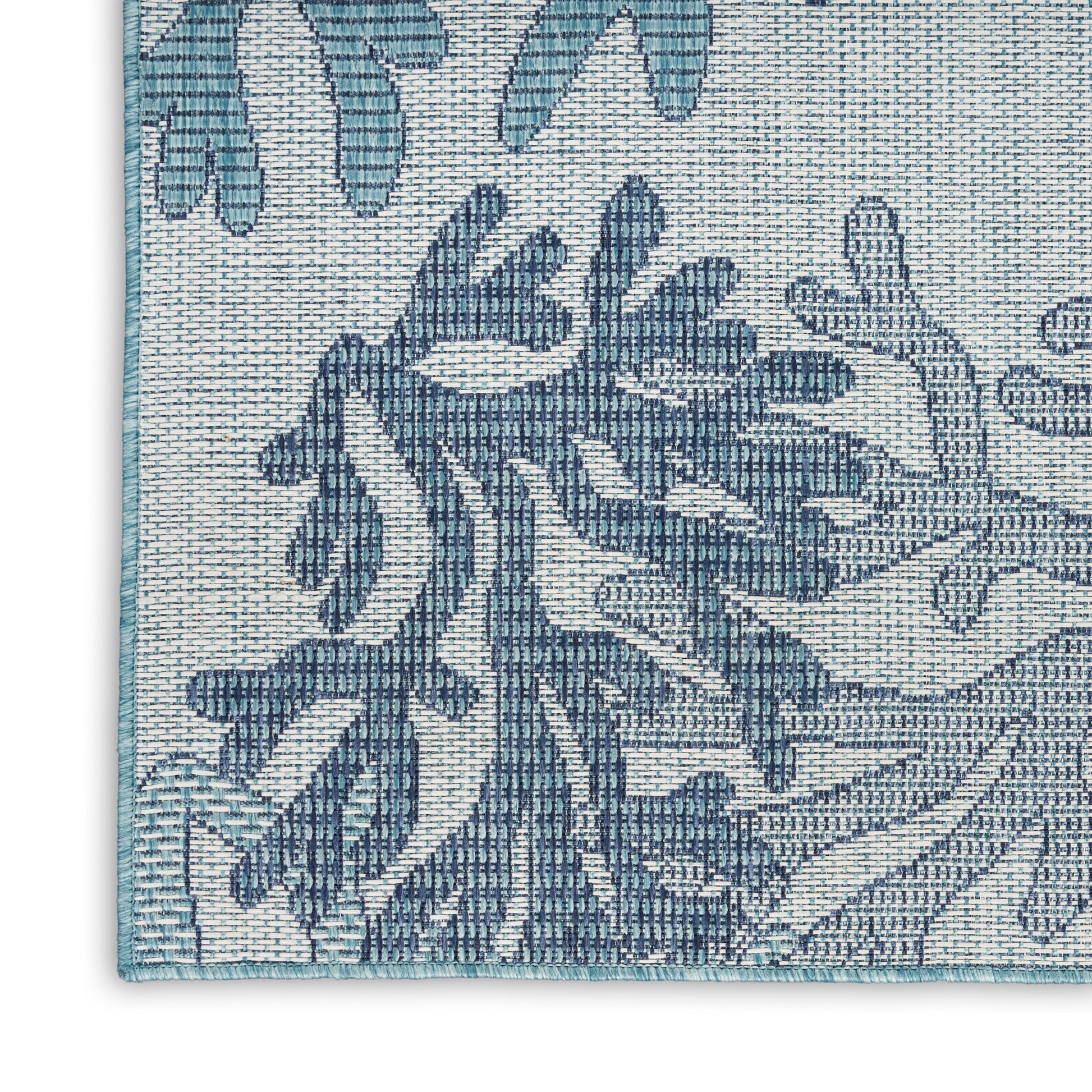 Blue damask-pattern woven rug corner with teal edge trim on beige background.