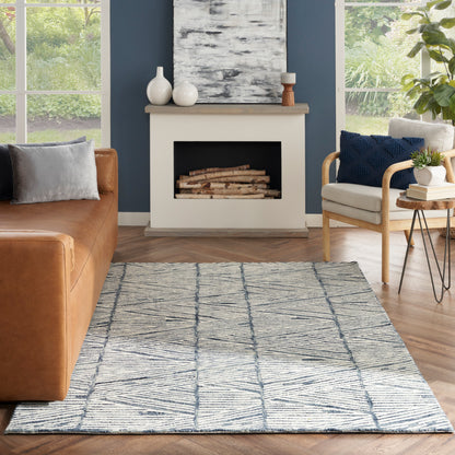 Blue-gray geometric area rug on wood floor in a cozy living room with a tan leather sofa, cream armchair, and fireplace.