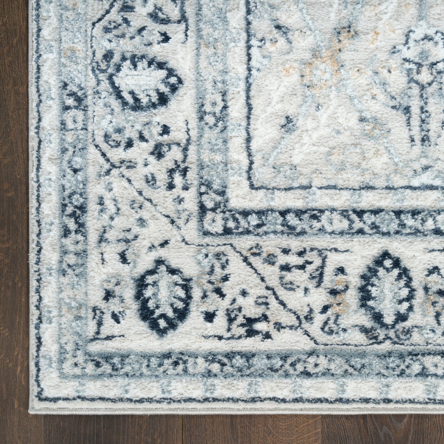 Blue and ivory oriental rectangular area rug with floral border and distressed pattern on dark wood floor.
