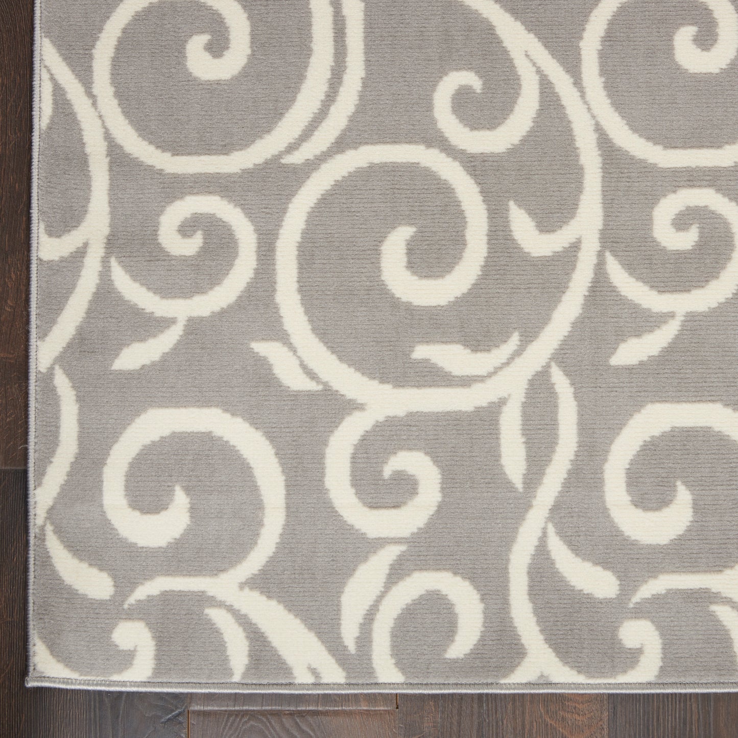 Gray area rug with white scroll swirl pattern; rectangular rug on dark wood floor.