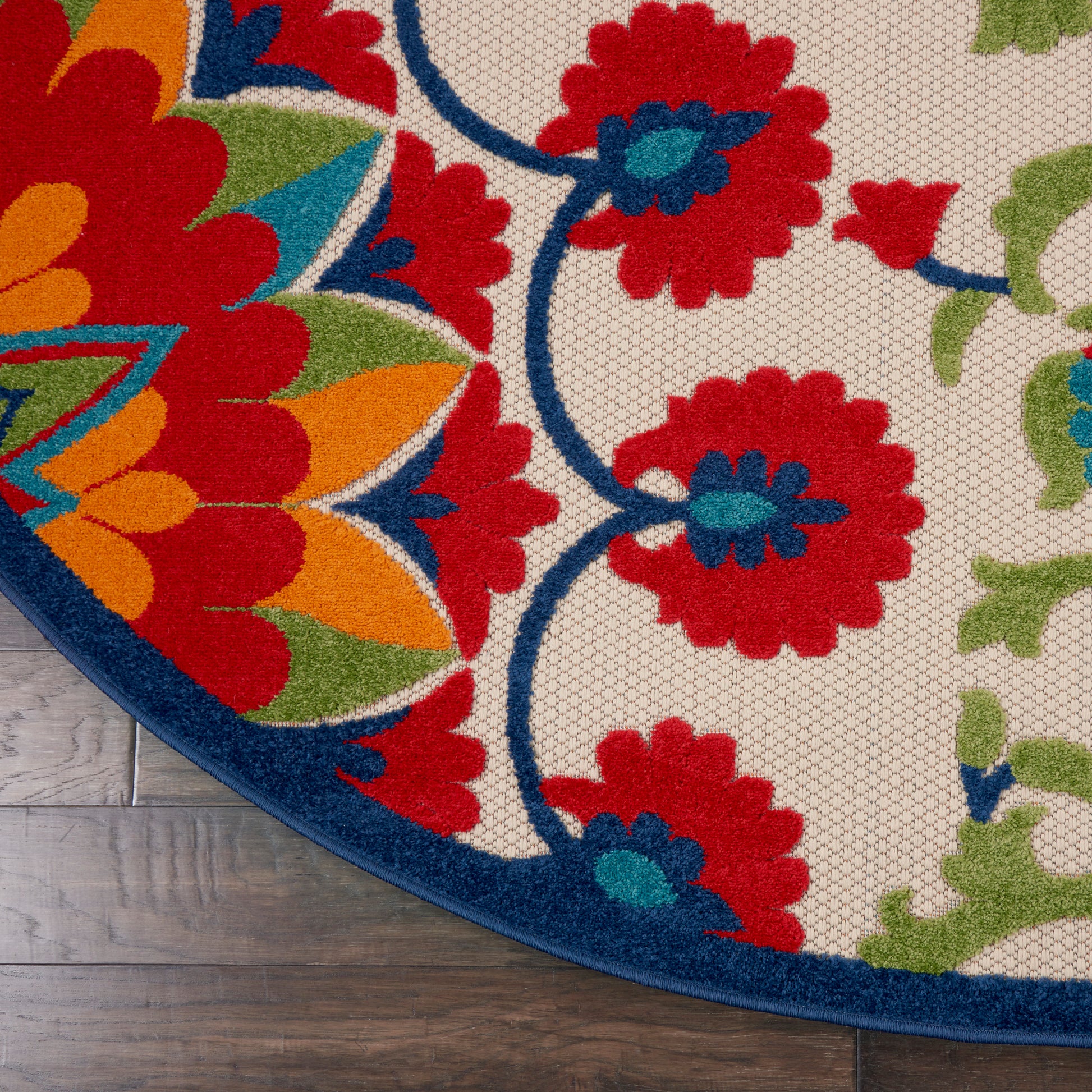 Round area rug with vibrant red, teal, blue and orange floral pattern on beige; deep blue border.