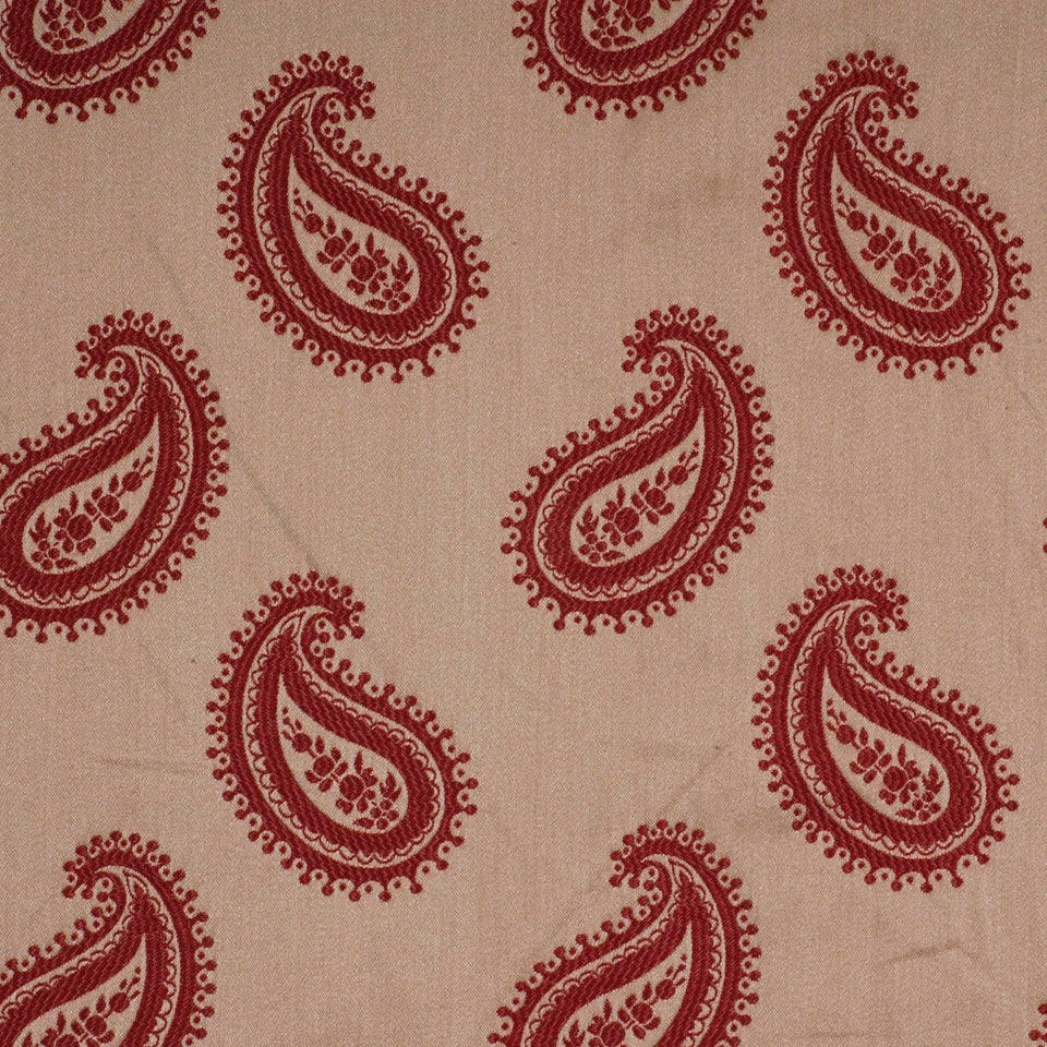 Tan fabric with repeating maroon paisley motifs and dotted borders; decorative textile.