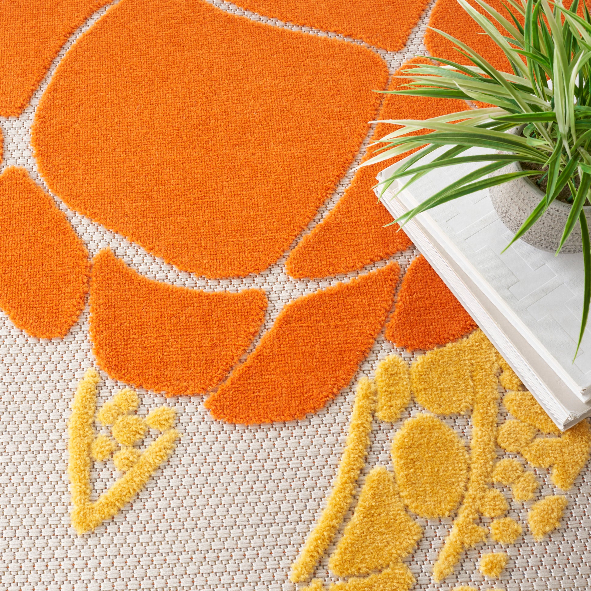 Bright orange and yellow plush rug with petal-like shapes on a beige base; round, cozy shag rug with a plant nearby.