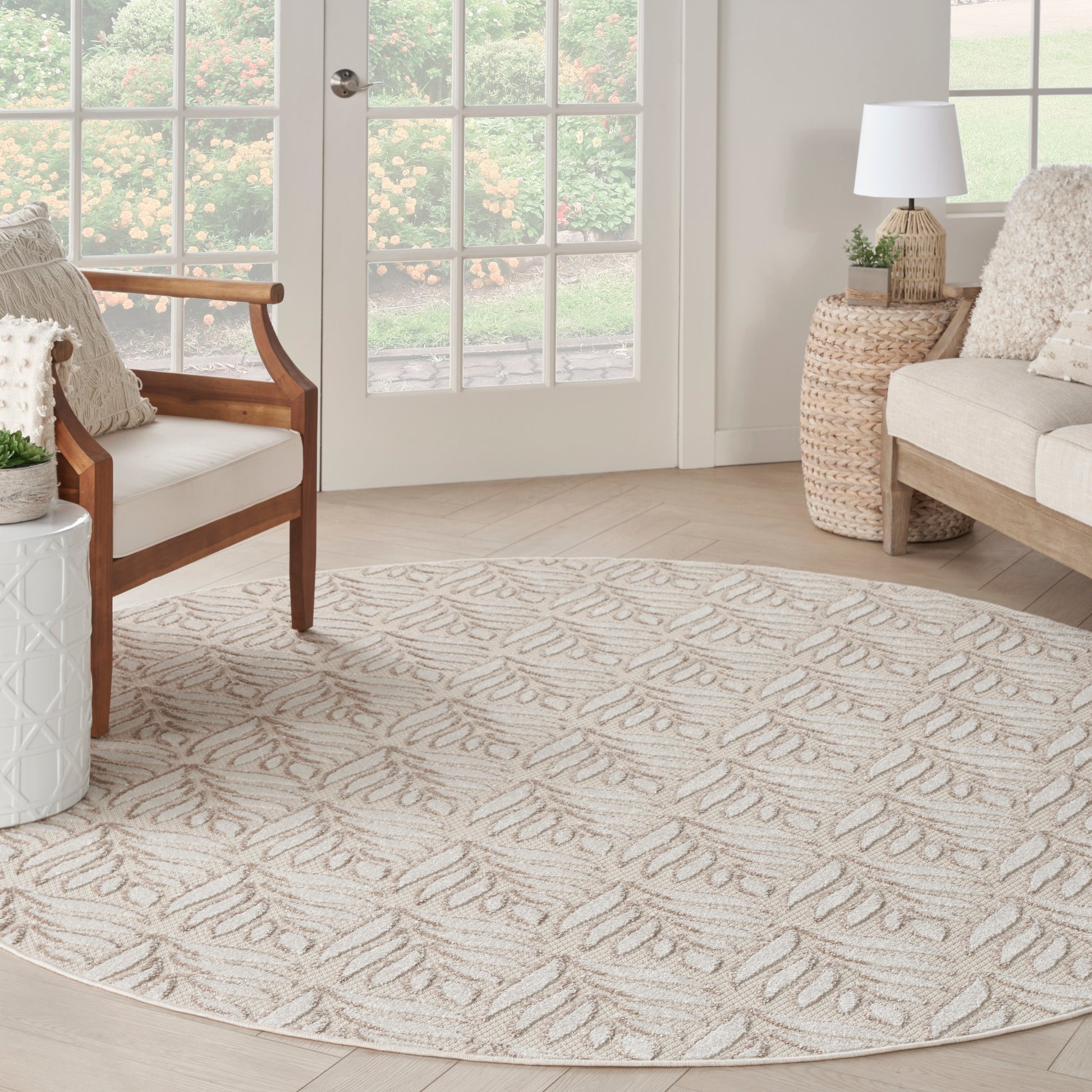 Round beige rug with a soft woven texture and ivory leaf pattern, in a bright neutral living room.