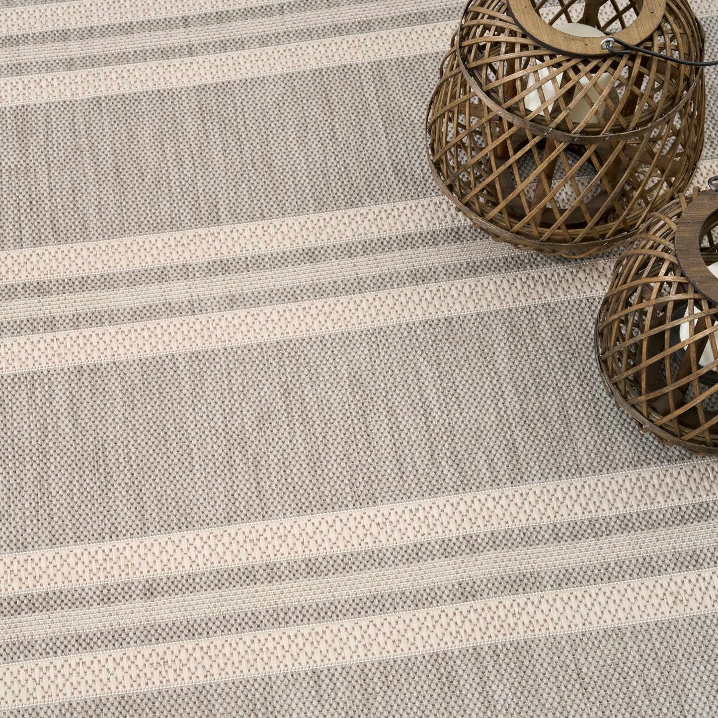 Grey striped woven rug with two round brown wicker lanterns, modern decor.