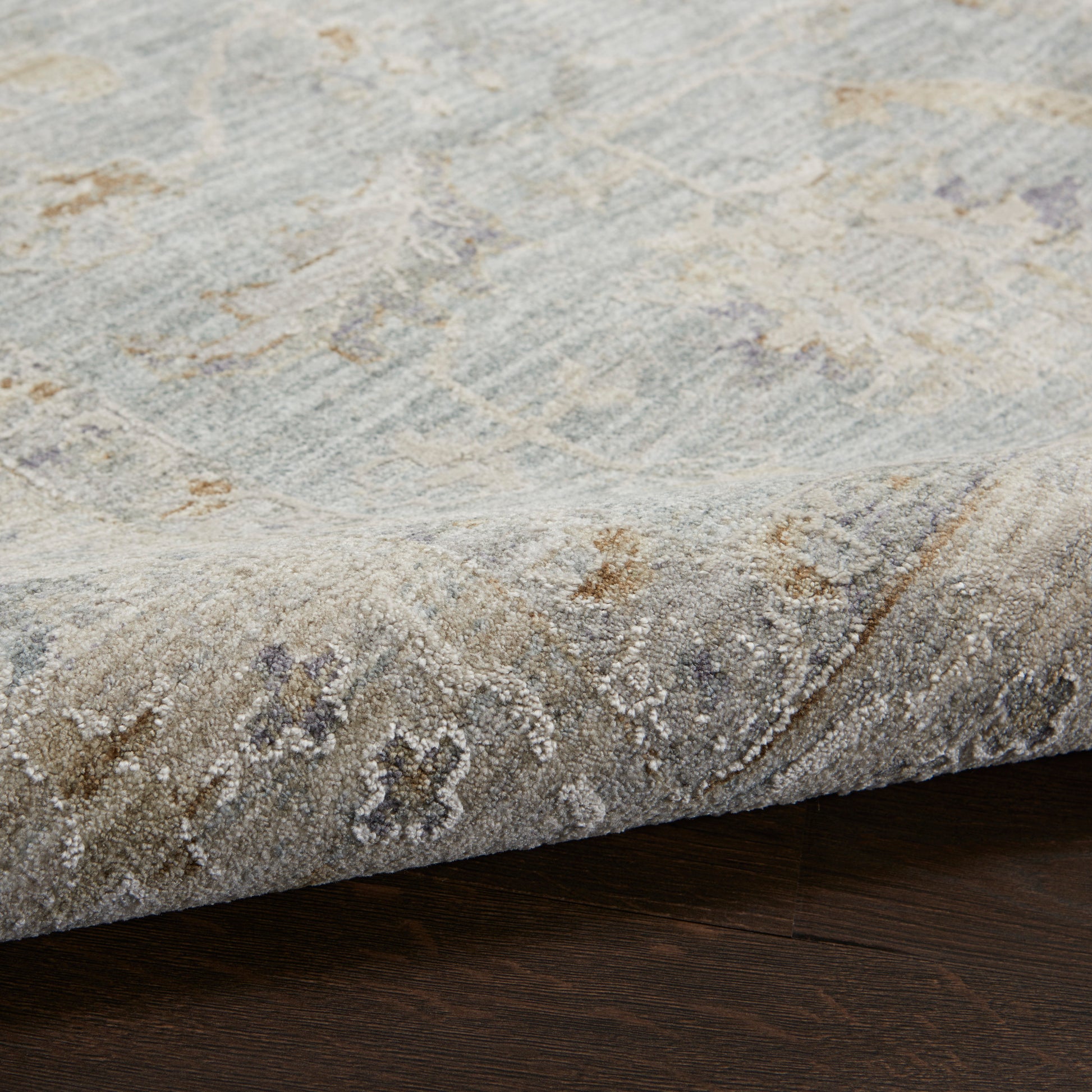 Blue-gray distressed area rug with ivory & tan floral motifs, soft textured pile, edge curling on dark wood floor.