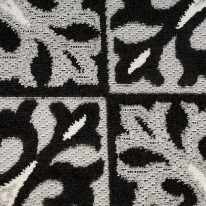 Close-up of a black and ivory tufted rug with floral geometric panels in a tiled grid.
