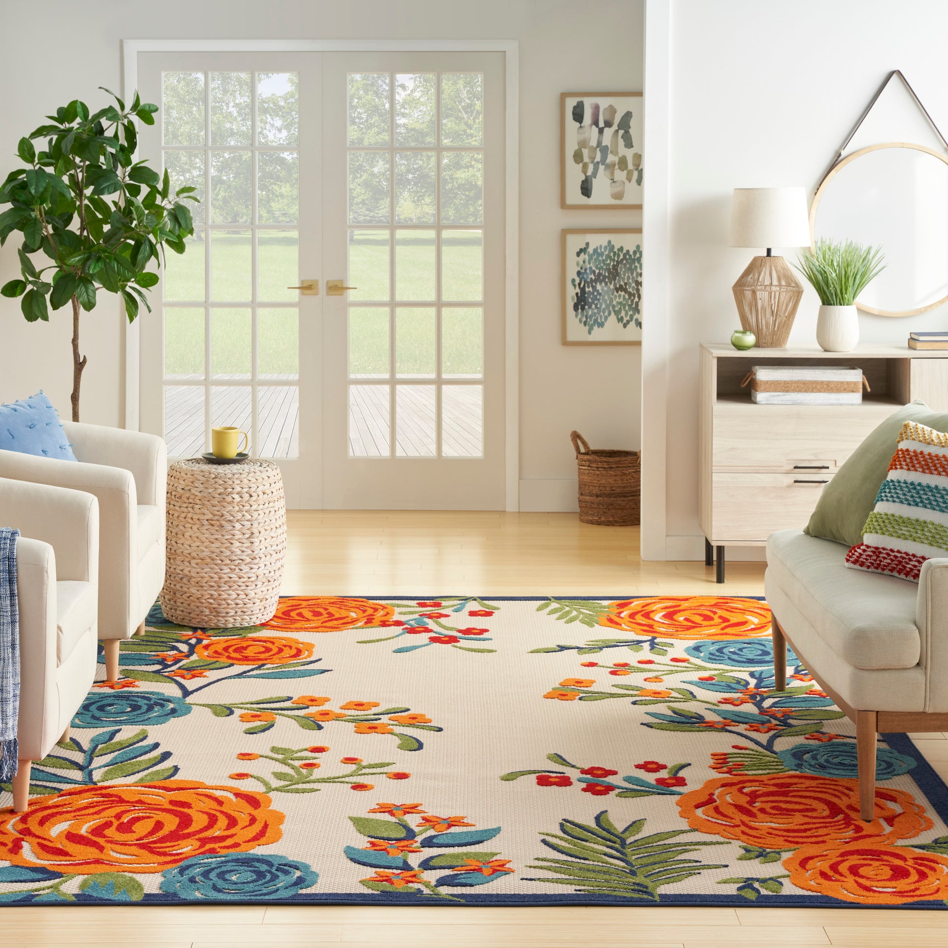 Bright living room with a colorful floral rug, cream sofas, wicker side table, and French doors.