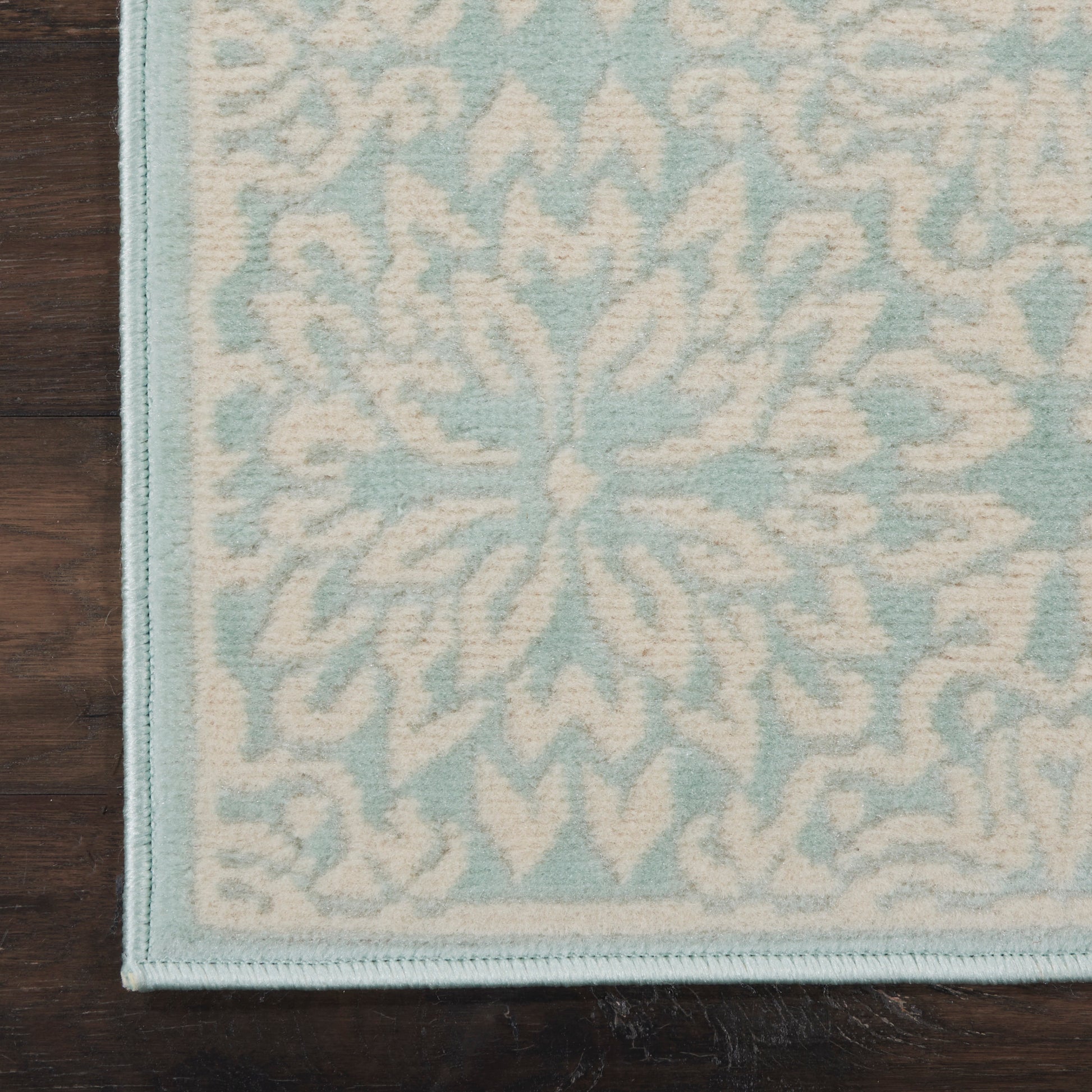 Light blue and white patterned area rug with a floral motif, soft pile, pale border, on dark wood floor.