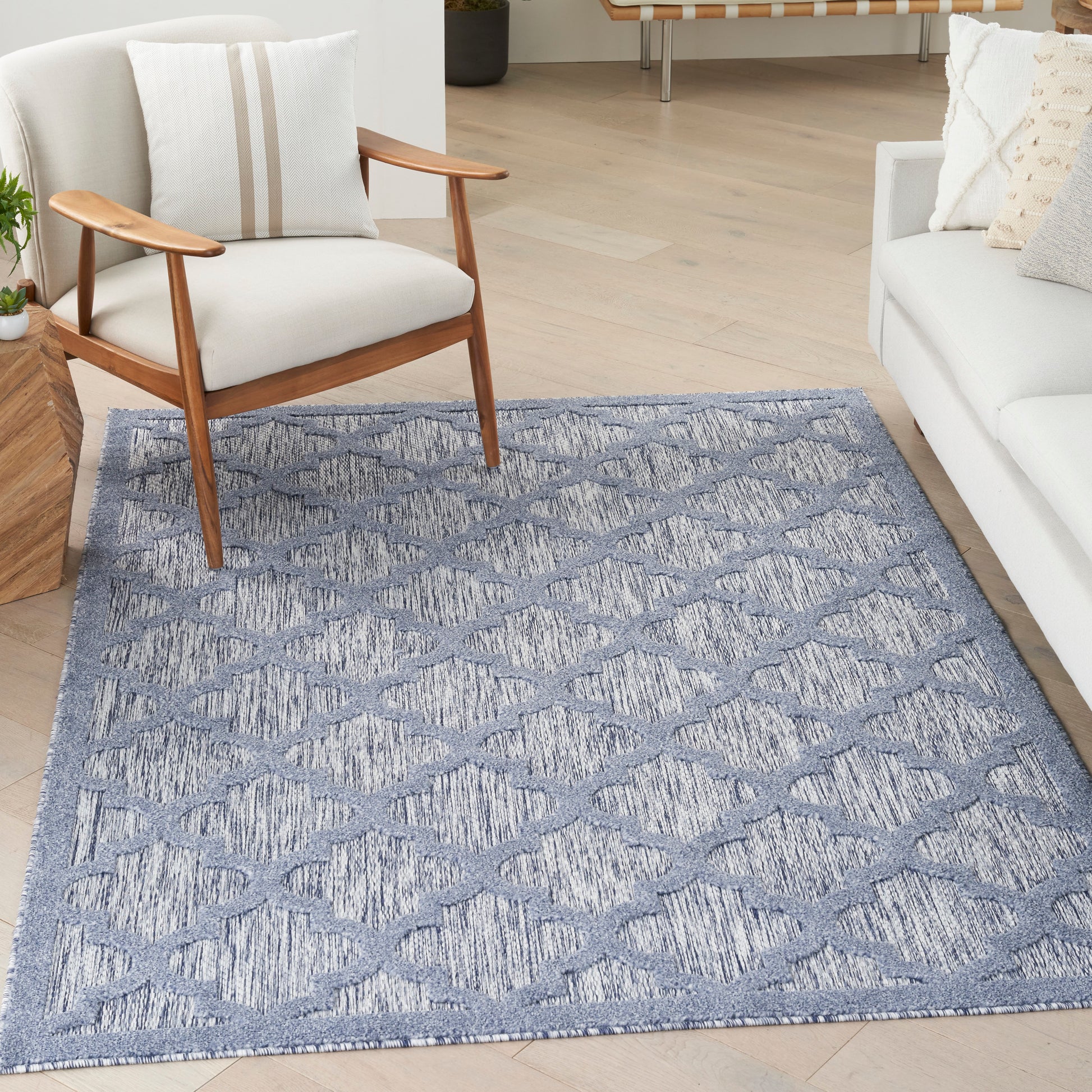 Blue-gray geometric diamond-pattern area rug in a modern living room with a wooden-armchair and white sofa.
