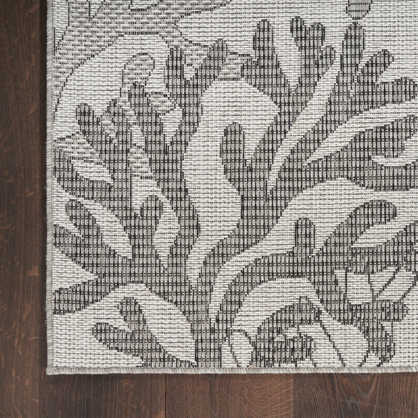 Neutral woven area rug with charcoal botanical pattern on ivory, edge visible on dark wood floor.