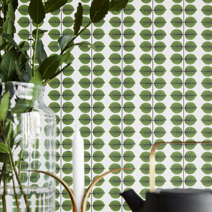 Green leaf-pattern wallpaper with vertical rows; foreground glass vase with stems and a black pot.
