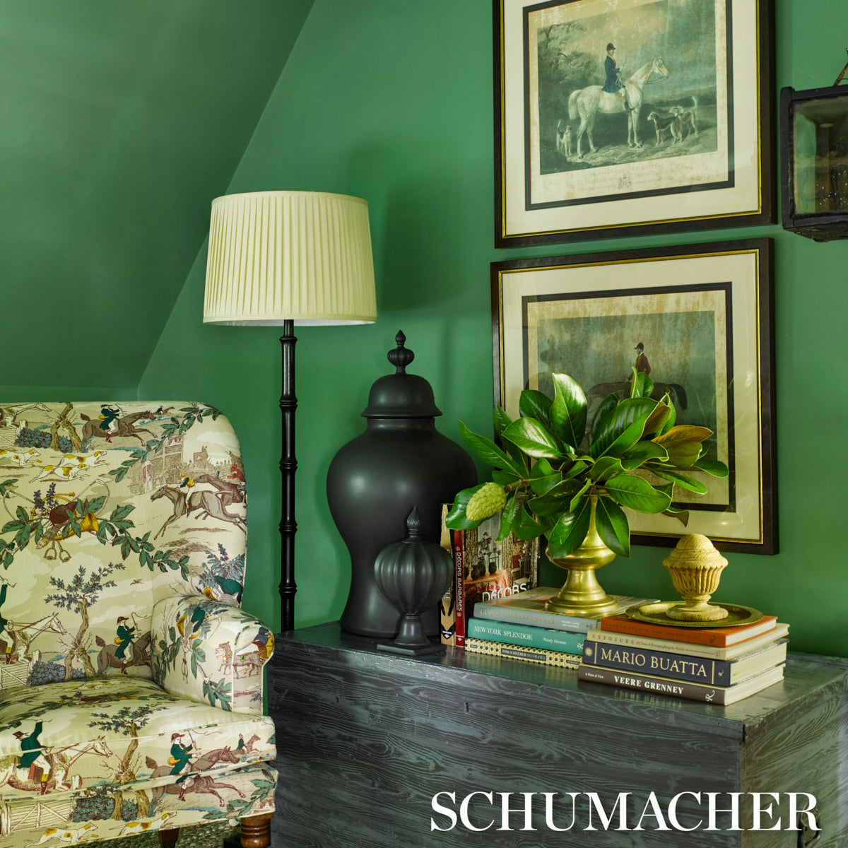 Green-walled room with a floral upholstered chair, black floor lamp, dark wood sideboard, brass planter and horse artworks.