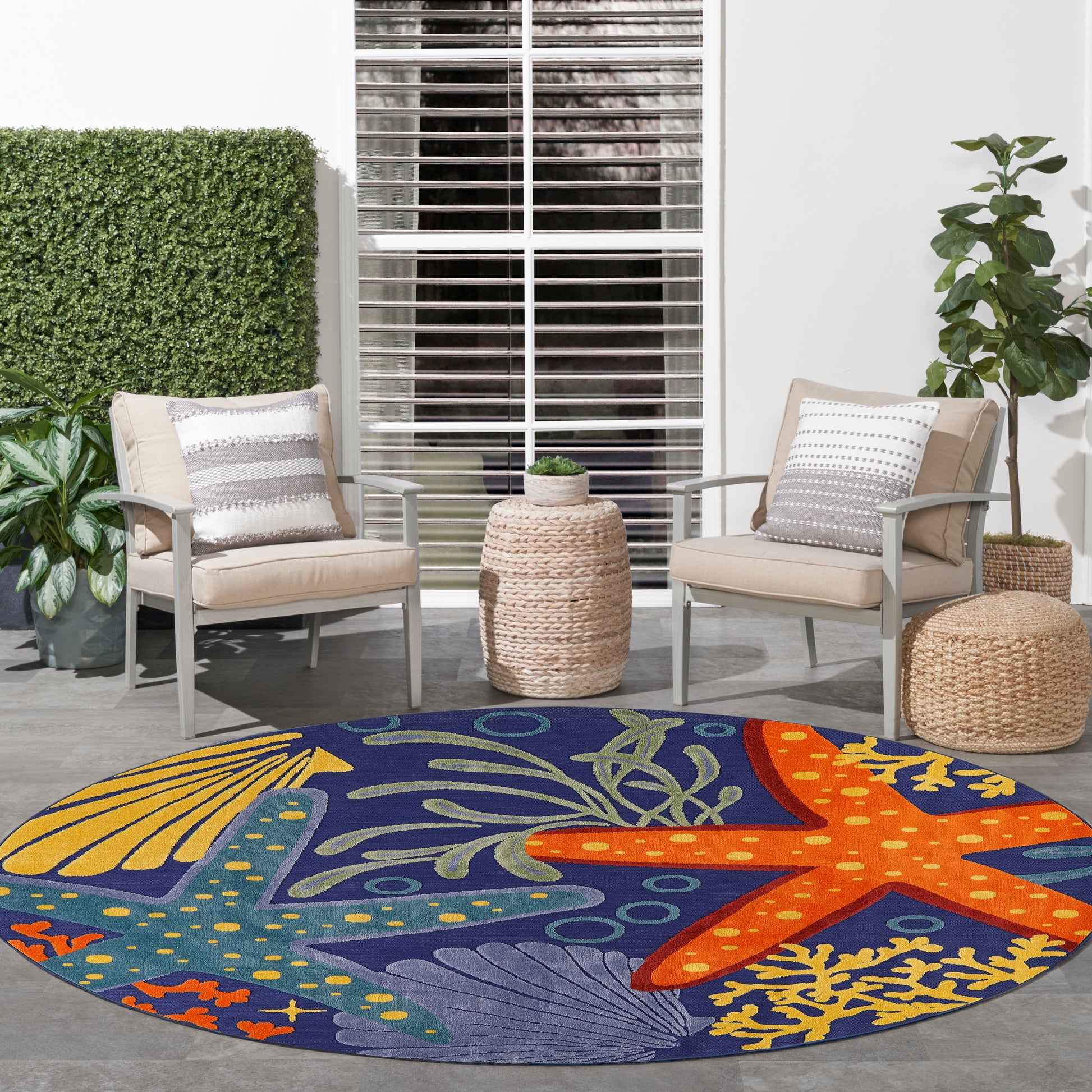 Round outdoor rug with navy background & colorful sea life pattern (starfish, coral) under beige cushioned patio chairs.