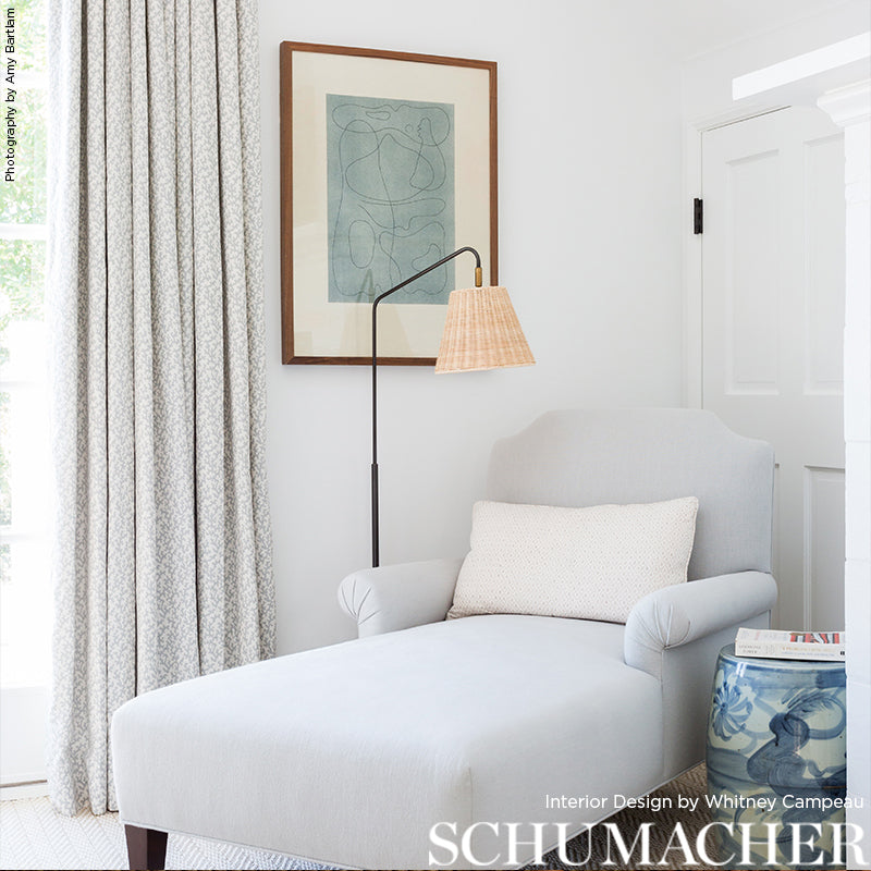 Light gray upholstered lounge chair with matching ottoman, beige pillow, arc floor lamp with woven shade, teal abstract art, patterned curtains