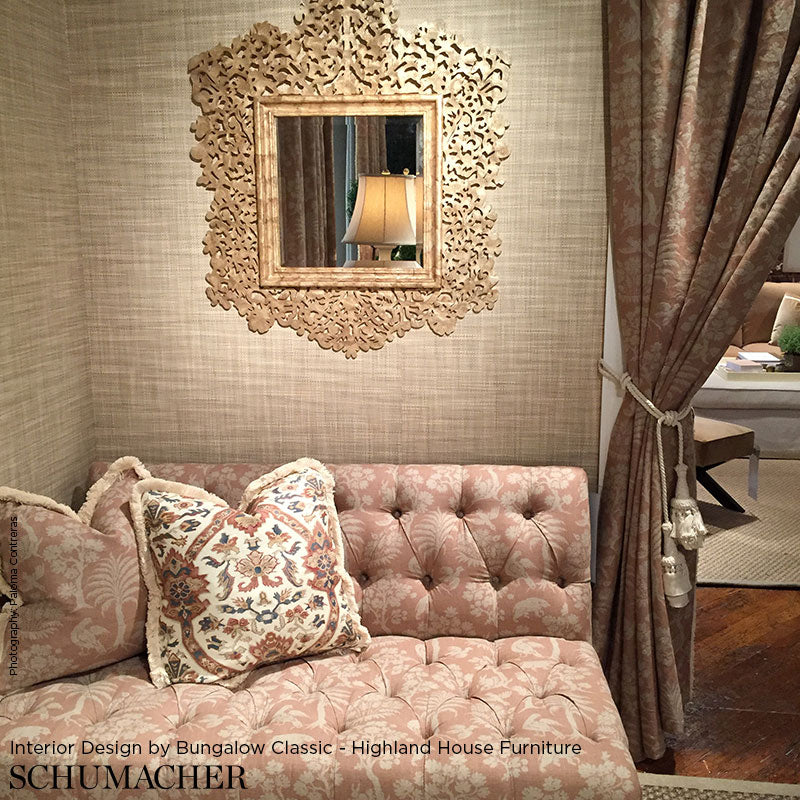Pink tufted velvet sofa with floral cushions, ornate carved-mold mirror, beige textured walls & tasseled drapes.