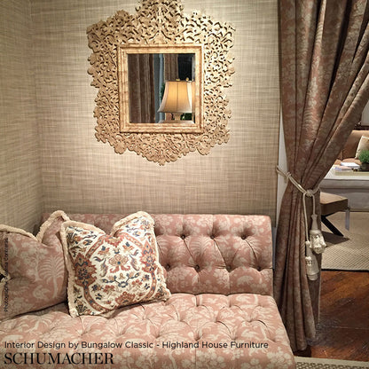 Pink tufted velvet sofa with floral cushions, ornate carved-mold mirror, beige textured walls & tasseled drapes.