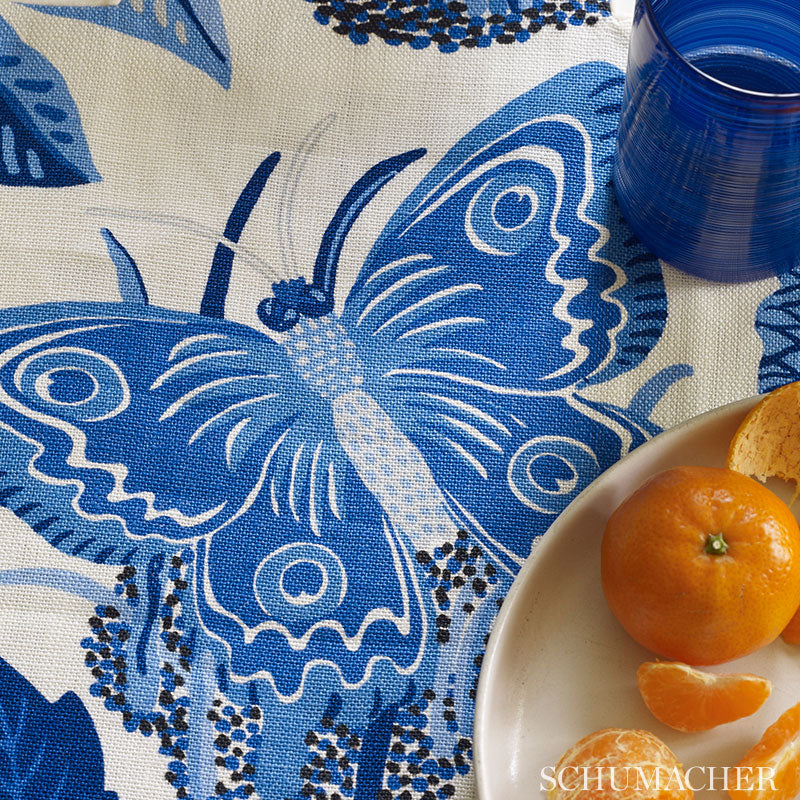Beige textile with a large blue butterfly motif; plate with orange and a blue glass nearby.