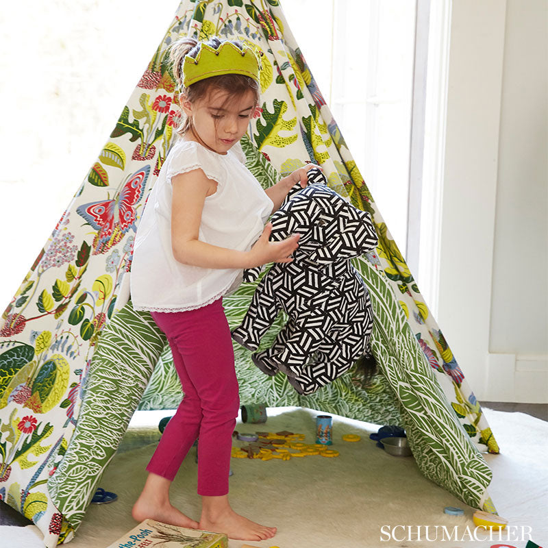 Colorful fabric with leafy and butterfly print; child in white top and magenta pants holds a black-and-white geometric bag.