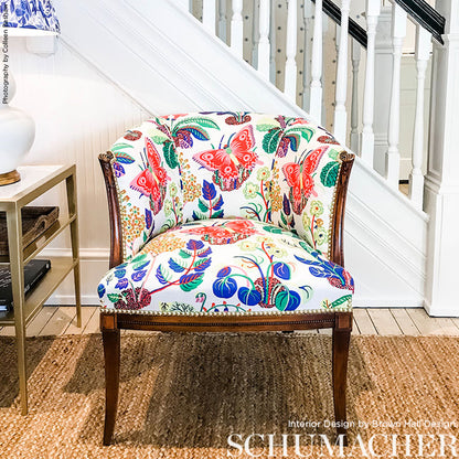 Colorful floral and butterfly upholstered armchair with dark wood legs and brass nailhead trim under a staircase.