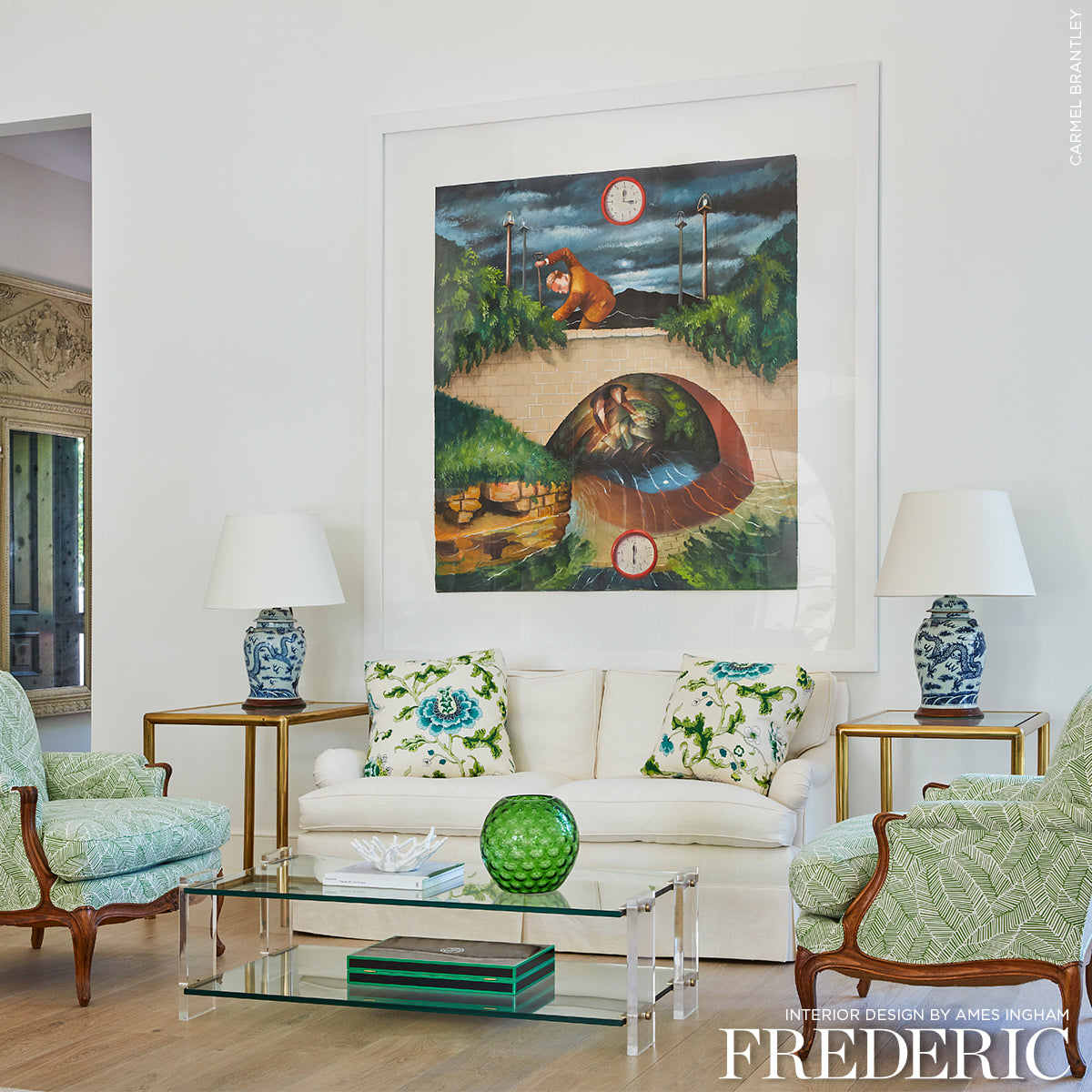 Bright living room with white sofa, floral cushions, glass coffee table, blue and white ceramic lamps, and abstract leaf prints on the wall.