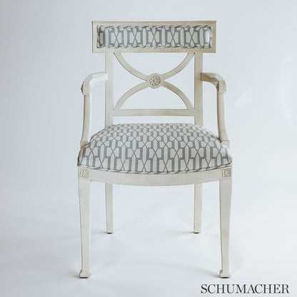 Distressed white wood armchair with blue geometric upholstery on seat and back, carved back panel and tapered legs.
