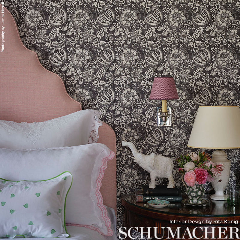 Pink velvet headboard with scalloped edge, damask black wallpaper, white lace-trimmed pillows, brass lamp, floral bouquet on nightstand.