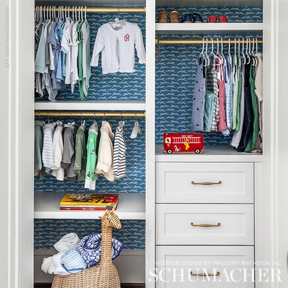 White wardrobe with a blue leopard-print backing, kids' clothes on rods, woven basket of blankets, a red toy fire truck, and white drawers.