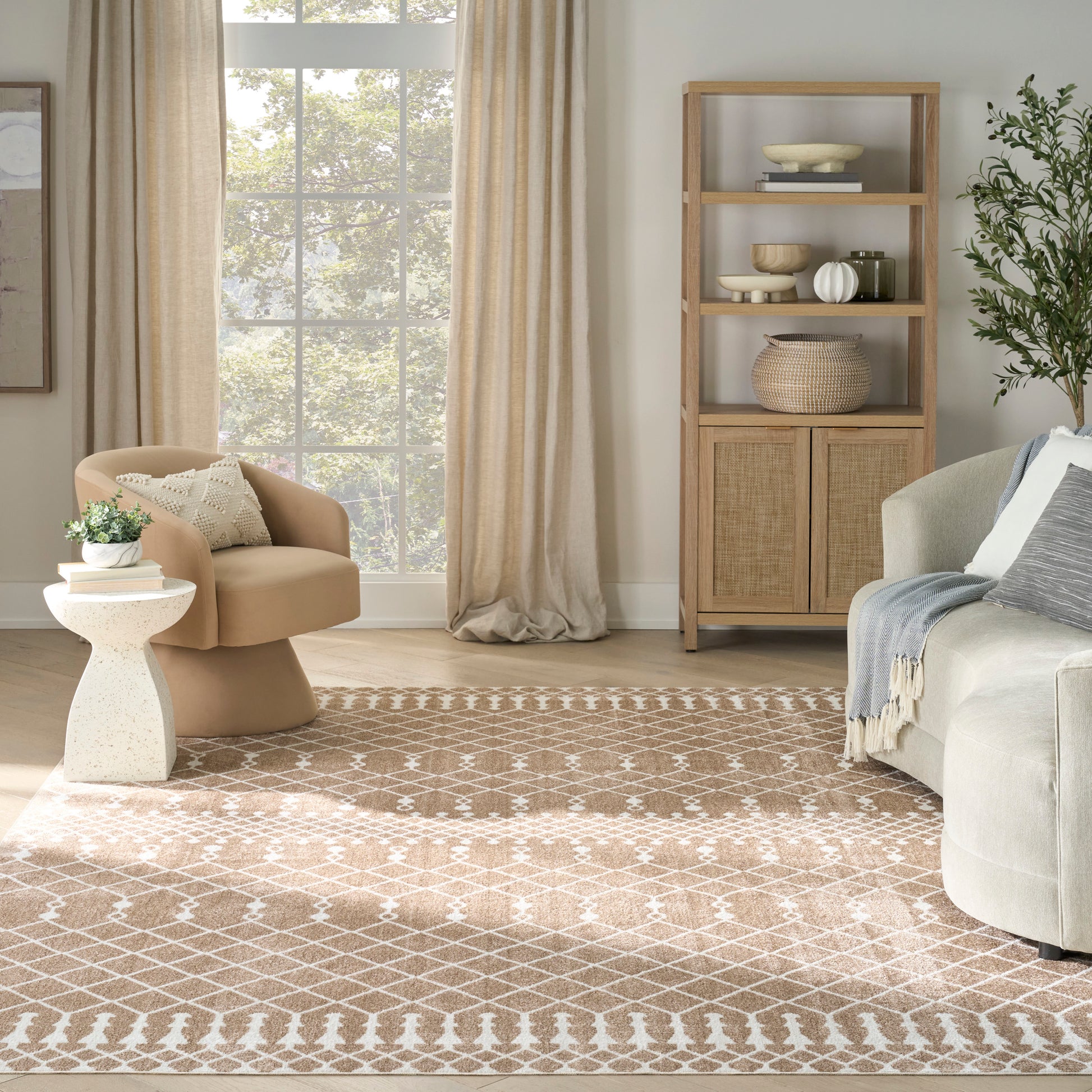 Neutral living room with large window, beige armchair, round terrazzo side table, light wood bookcase, and tan rug.