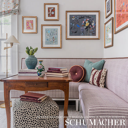 Cottage-style living room with wooden coffee table, polka-dot ottoman, lilac sofa, framed art, teal vase & books.