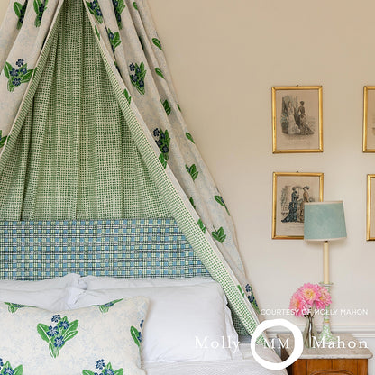 Green block-printed canopy over a blue plaid upholstered bed, white linens and botanical pillows in a vintage-style bedroom.
