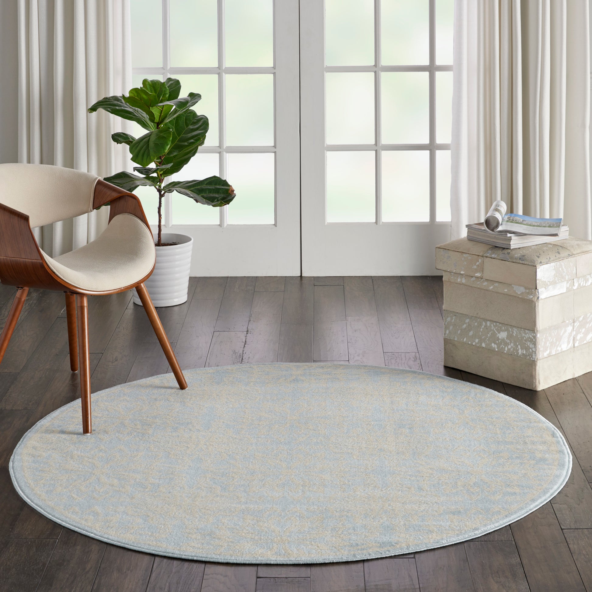 Round light blue-gray woven rug in a modern living room with a wood chair, plant, and stack of decorative blocks.