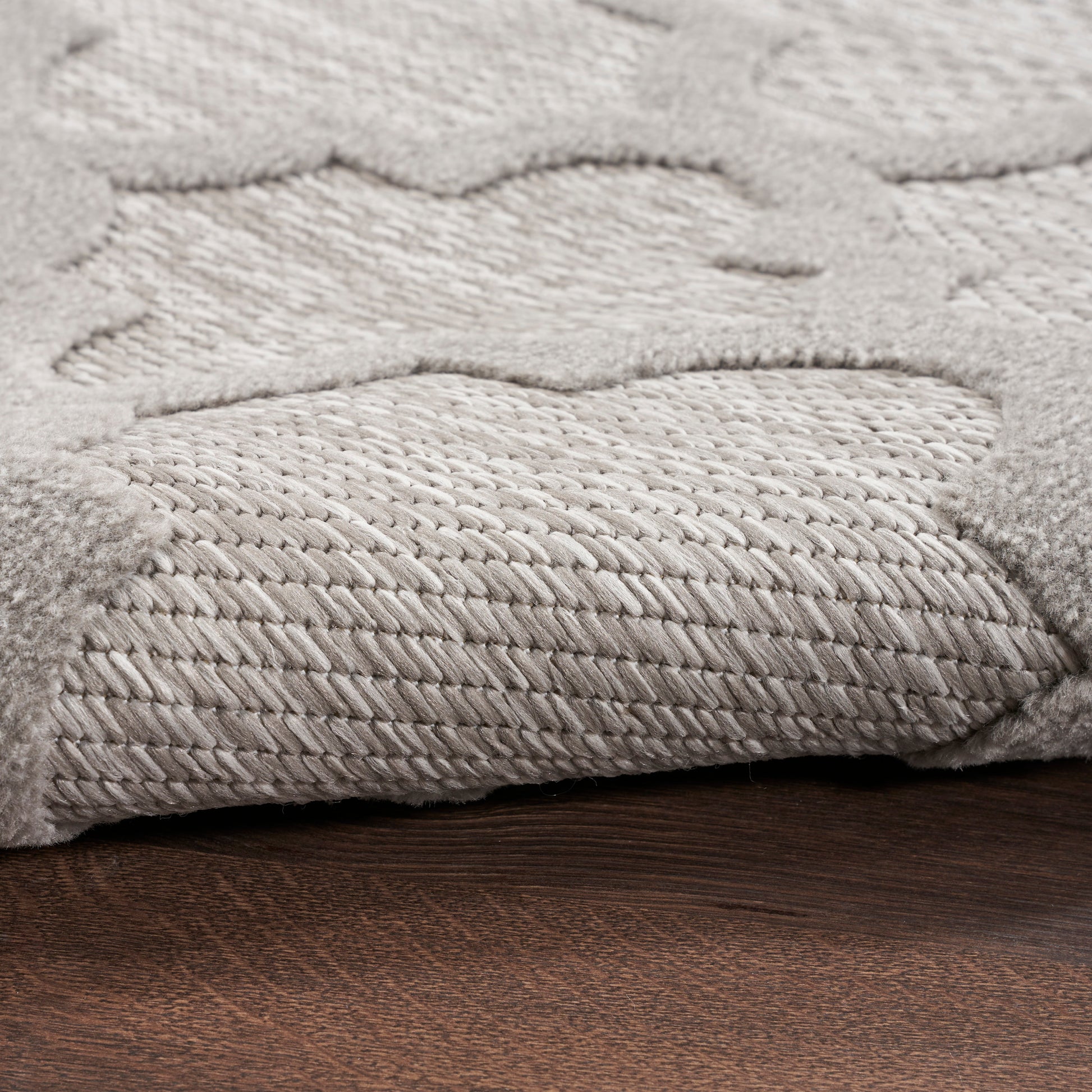 Light gray plush rug with raised cloud-like pattern and braided border on dark wood floor.