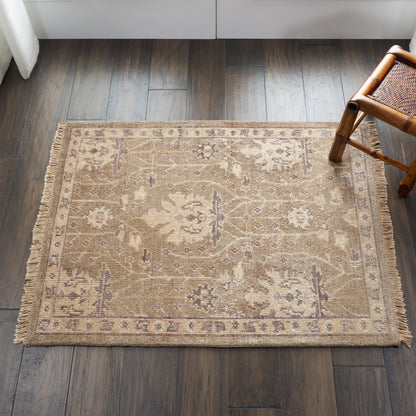 Beige oriental-style rug with floral motifs and fringed borders on dark hardwood floor, near a wicker chair.
