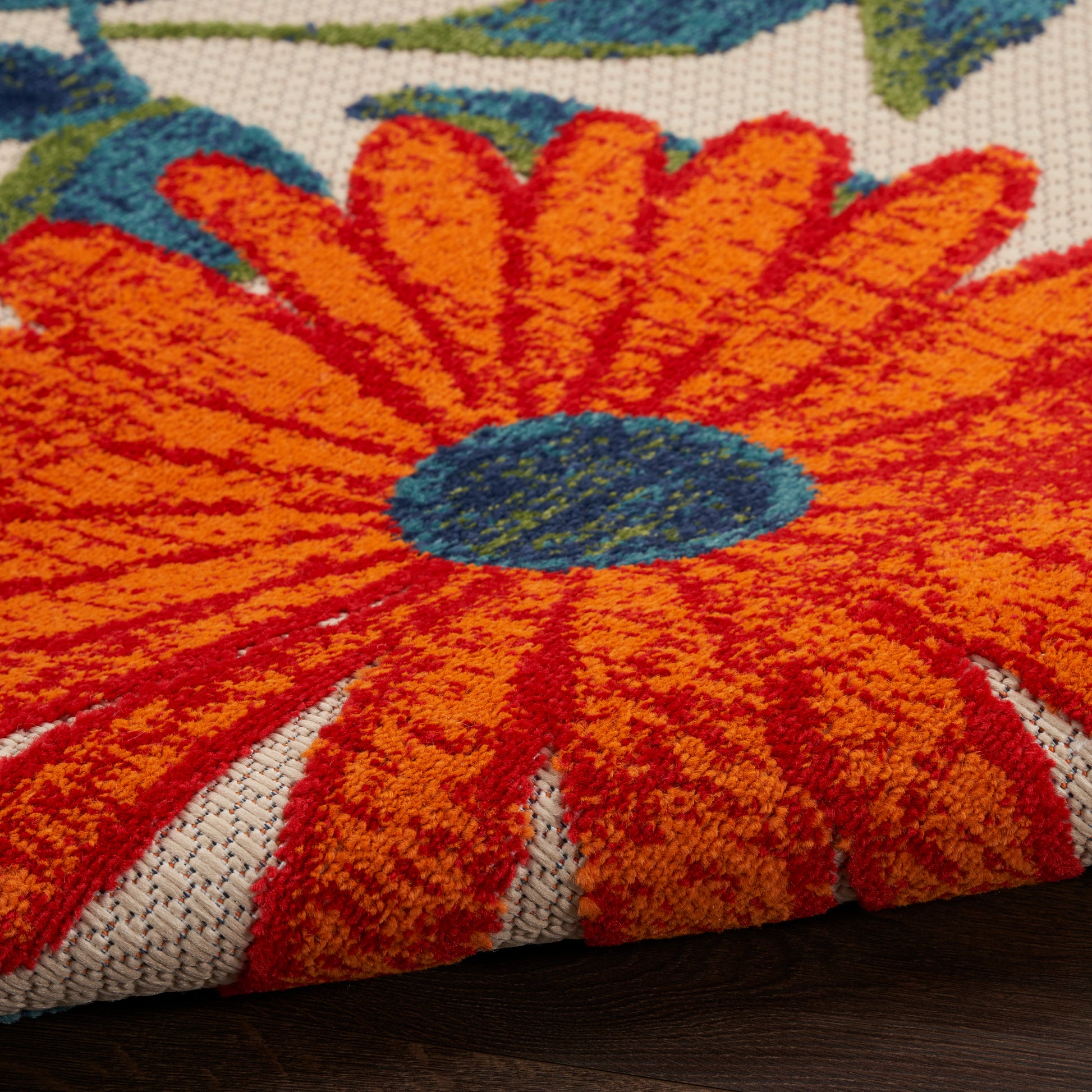 Close-up of a bold floral rug with orange petals and blue center; high-pile tufted on beige woven backing.