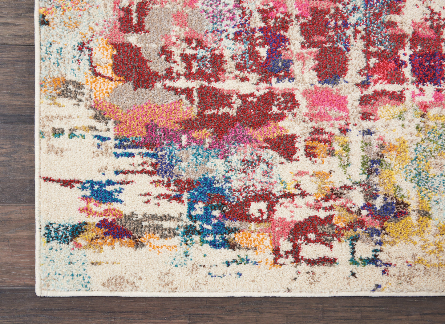 Abstract multicolor tufted rug on dark wood floor; cream base with red, pink, blue, yellow and teal patches.