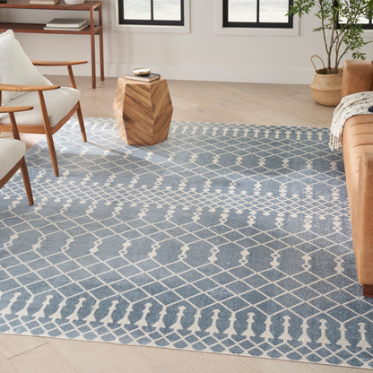 Rectangular blue geometric area rug with white lattice pattern in a modern living room; wood furniture, plant, and tan sofa.