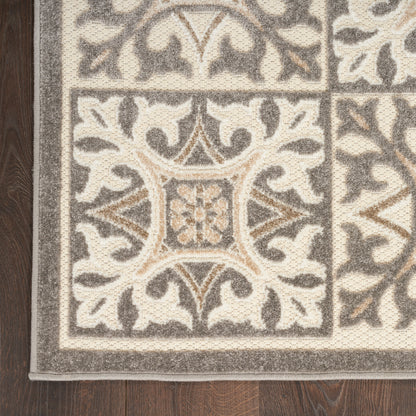 Beige and gray ornate area rug with floral scroll motif and double border on dark wood floor.