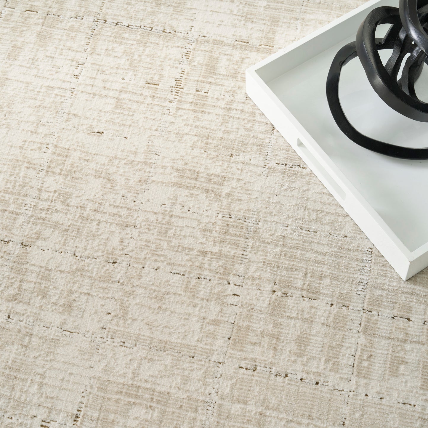 Beige woven rug with a white tray and a black circular metal sculpture in the corner.