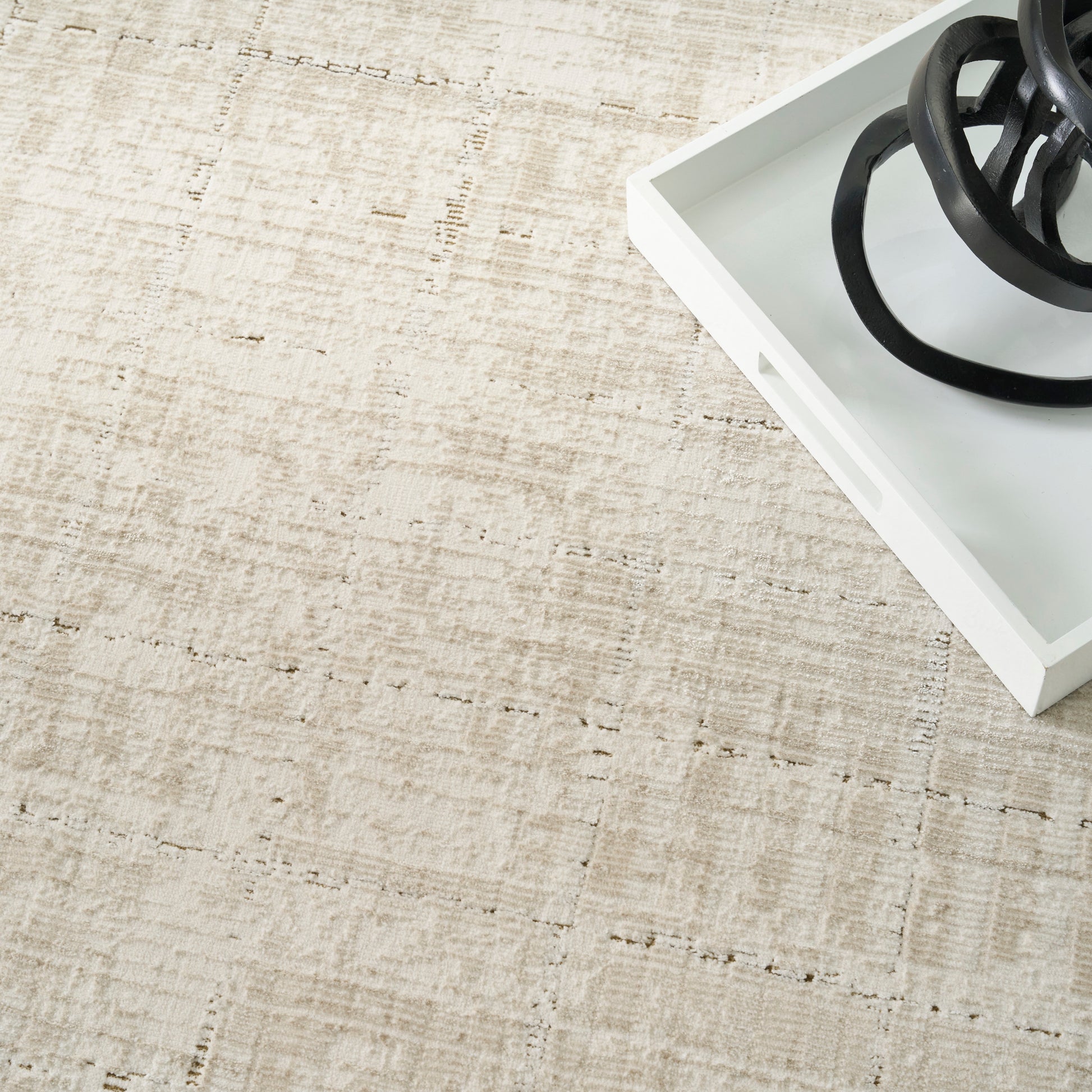 Beige woven rug with a white tray and a black circular metal sculpture in the corner.
