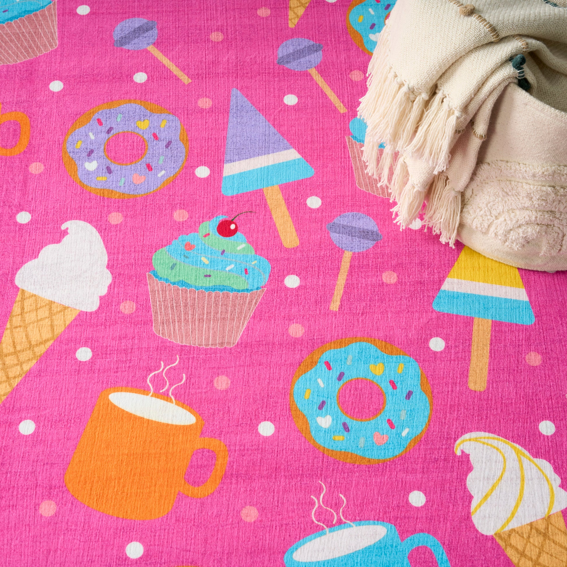 Bright pink dessert-print kid's rug with donuts, cupcakes, ice cream cones and popsicles; beige fringe at edge.