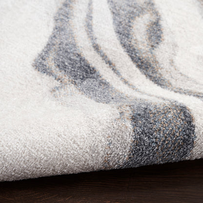 Soft gray rug with abstract dark blue-gray pattern, folded edge showing plush texture on dark wood floor.