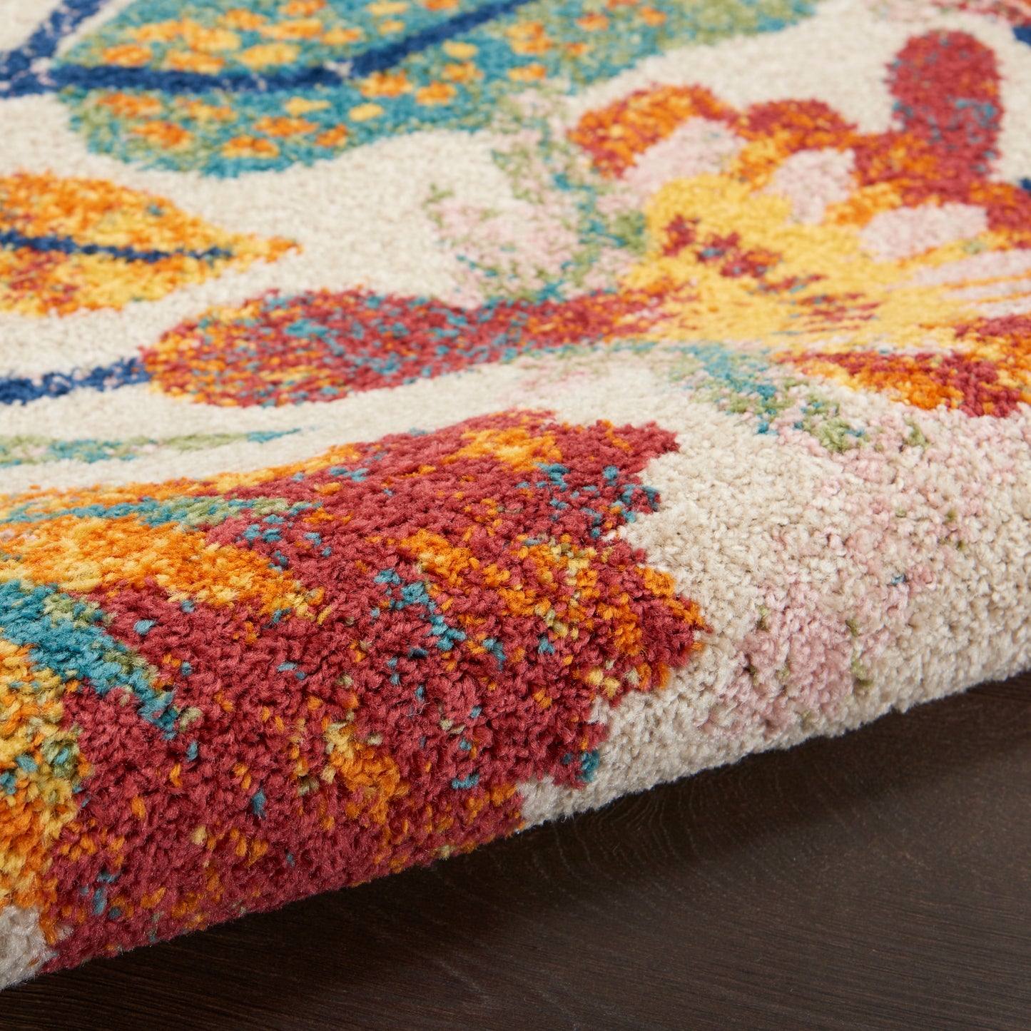 Close-up of a plush, multicolor tufted rug with red, orange, teal and pink patterns on a dark wood floor.