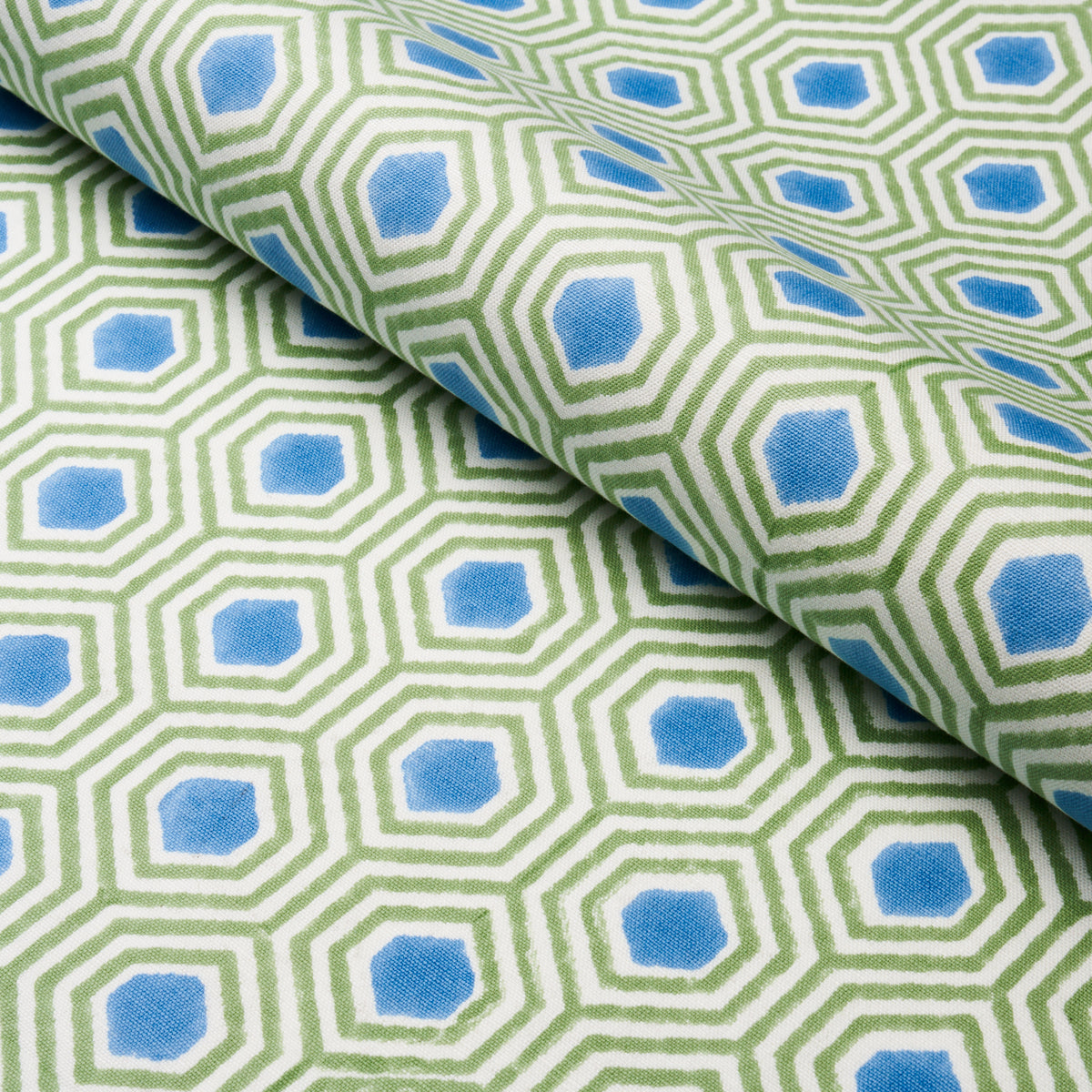 Green hexagonal lattice pattern with blue centers on a light background, folded cotton fabric.