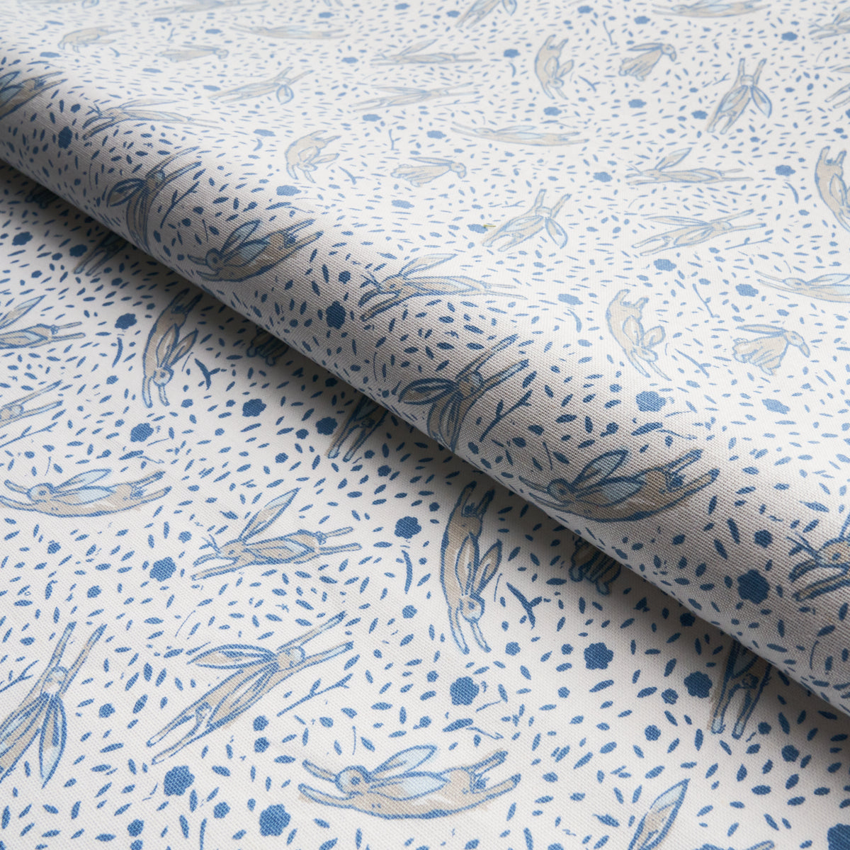White fabric with a pale blue rabbit print and tiny dot motifs; airy cottage-style textile.