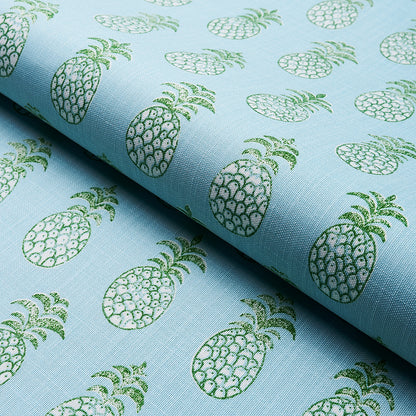 Light blue fabric with a repeating green pineapple print, folded on a roll.