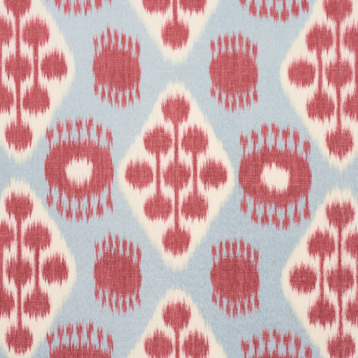 Blue woven fabric with pink-red ikat-inspired diamonds and circular motifs; boho textile for cushions or curtains.