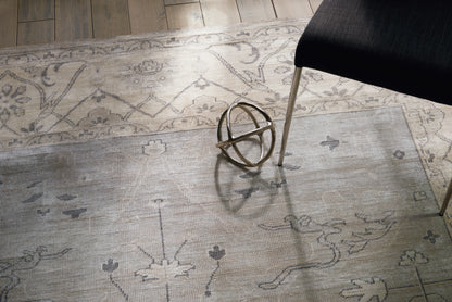 Light gray patterned area rug with floral motifs; a metallic geometric orb sculpture sits near a black chair with metal legs.