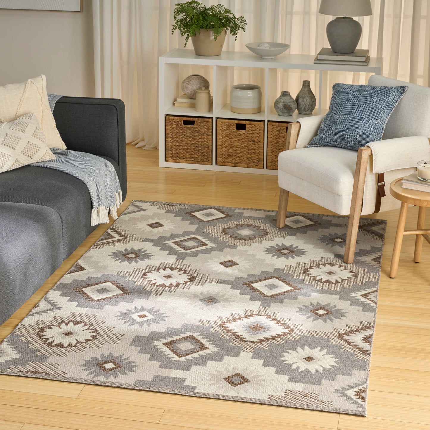 Geometric gray-beige area rug on a light wood floor in a cozy living room with a dark blue sofa, light armchair, and wicker baskets.