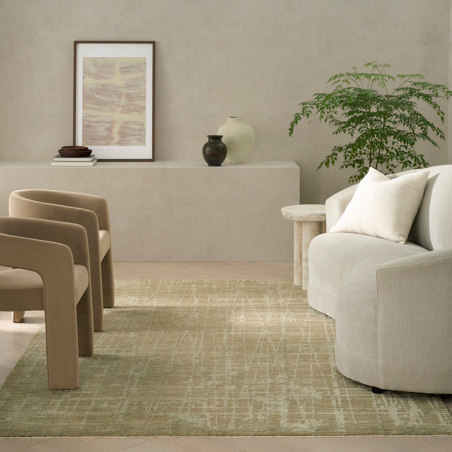 Neutral living room with beige curved chairs, cream sofa, sage green patterned rug, framed art, vases, and potted plant.
